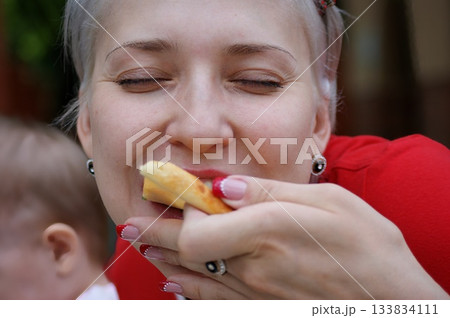 One blonde girl bites and eats pizza, she closed her eyes with pleasure and smiles. One blonde girl bites and eats pizza, she closed her eyes with pleasure and smiles. 133834111