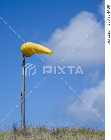 Yellow wind sock blowing in strong wind against sky 133834499