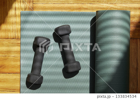 Overhead view of partially rolled yoga mat and weights on wooden floor Overhead view of partially rolled yoga mat and weights on wooden floor 133834534