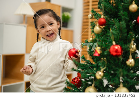 toddler girl holding a toy ball. decorating the Christmas tree at home 133835452