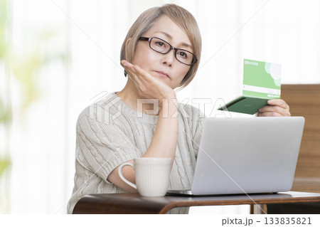 リビングで通帳とパソコンをにらめっこするシニア女性 133835821