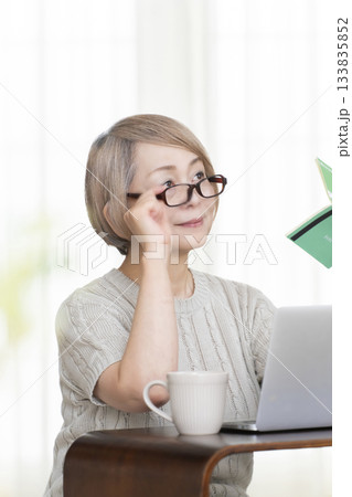 リビングで通帳とパソコンをにらめっこするシニア女性 133835852