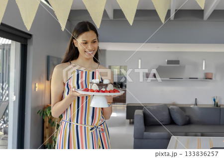 Woman holding cake stand in modern kitchen with chocolate dessert, strawberries, copy space 133836257