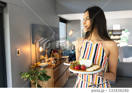 Asian woman holding platter with dip, crackers and strawberries in open kitchen, copy space 133836280