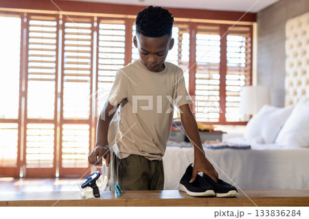 African American boy leaning over wooden bench picking up snorkel gear and shoes in bedroom African American boy leaning over wooden bench picking up snorkel gear and shoes in bedroom 133836284