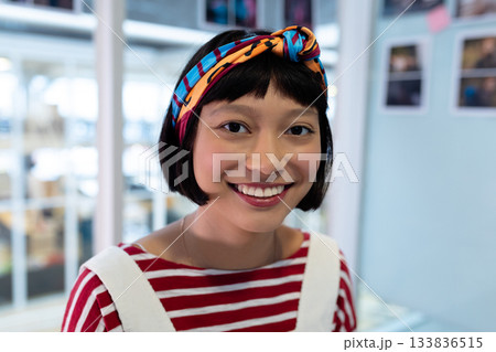 Adult Asian woman smiling wearing headband, striped shirt, necklace in studio with glass panels 133836515