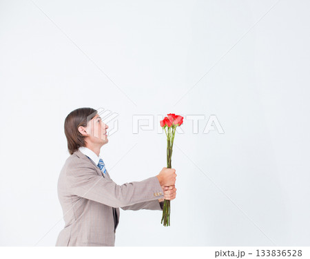 Man wearing grey suit and striped tie offering bouquet of red roses at studio, copy space Man wearing grey suit and striped tie offering bouquet of red roses at studio, copy space 133836528