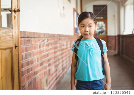 Asian female child standing in long school corridor wearing black backpack and passing wooden door Asian female child standing in long school corridor wearing black backpack and passing wooden door 133836541