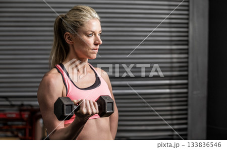 Mid adult woman wearing pink sports bra and holding hexagonal dumbbell in gym, copy space Mid adult woman wearing pink sports bra and holding hexagonal dumbbell in gym, copy space 133836546