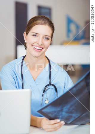 Female doctor examining radiograph film at clinic office workspace with laptop and stethoscope Female doctor examining radiograph film at clinic office workspace with laptop and stethoscope 133836547