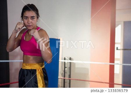 Female athlete standing in boxing ring raising fists wearing pink sports bra black shorts Female athlete standing in boxing ring raising fists wearing pink sports bra black shorts 133836579