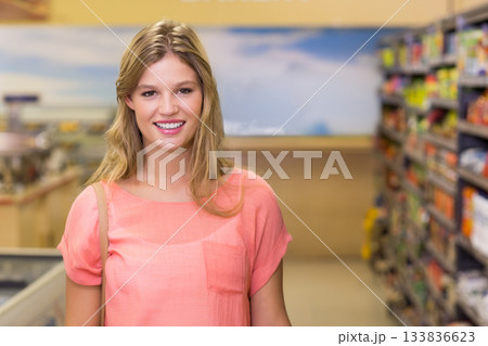 Woman carrying shoulder bag and smiling inside supermarket aisle by refrigerated display unit 133836623