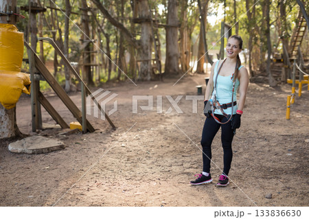 Woman navigating rope course in forest wearing harness with carabiners, gloves, copy space Woman navigating rope course in forest wearing harness with carabiners, gloves, copy space 133836630