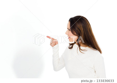 Woman pointing with right hand wearing white top in studio against blank background, copy space 133836633