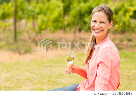 Woman wearing coral-pink shirt, sitting at vineyard edge holding glass of white wine, copy space Woman wearing coral-pink shirt, sitting at vineyard edge holding glass of white wine, copy space 133836648