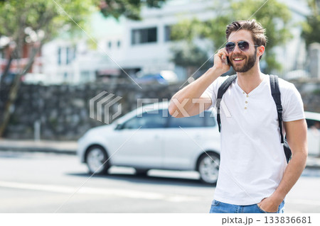 Man in his twenties calling on smartphone on sidewalk by stone wall wearing sunglasses, copy space 133836681
