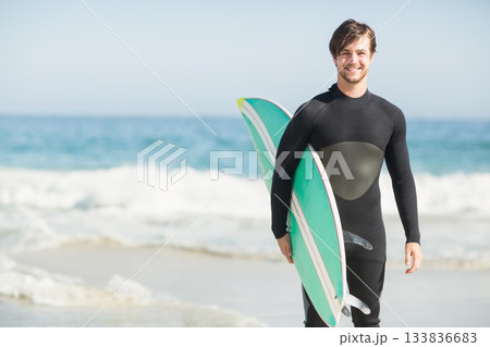 Male surfer emerging from waves at beach wearing wetsuit with green-white surfboard, copy space Male surfer emerging from waves at beach wearing wetsuit with green-white surfboard, copy space 133836683
