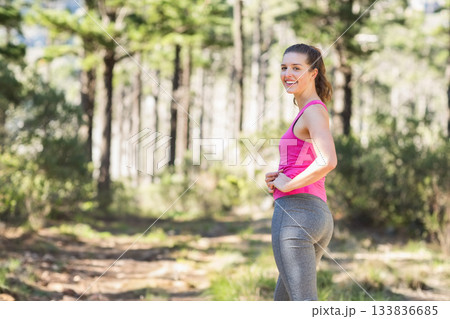 Athletic woman smiling on sunlit pine forest trail wearing fitted tank top and leggings, copy space 133836685