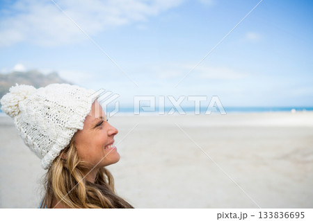 Woman standing at beach wearing white knitted pom-pom beanie and gazing toward ocean, copy space Woman standing at beach wearing white knitted pom-pom beanie and gazing toward ocean, copy space 133836695