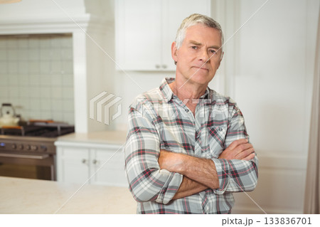 Senior man standing at kitchen countertop with arms crossed near tiled backsplash and gas stove Senior man standing at kitchen countertop with arms crossed near tiled backsplash and gas stove 133836701