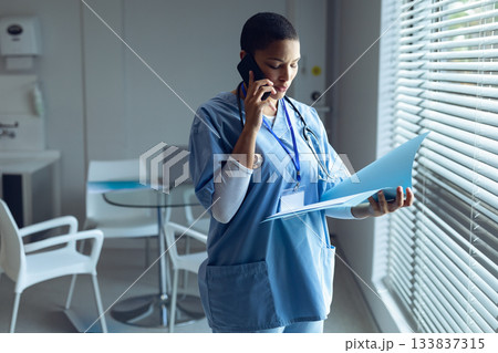 African American female nurse speaking on smartphone holding folder wearing stethoscope in clinic African American female nurse speaking on smartphone holding folder wearing stethoscope in clinic 133837315