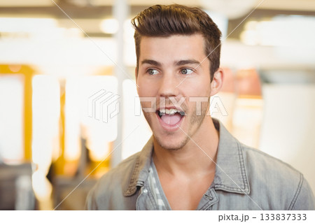 Man in twenties speaking with surprise in bright open-plan office under warm overhead lights Man in twenties speaking with surprise in bright open-plan office under warm overhead lights 133837333