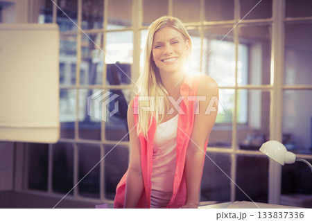 Smiling woman leaning forward on desk at office with flip chart, desk lamp and glass partition Smiling woman leaning forward on desk at office with flip chart, desk lamp and glass partition 133837336