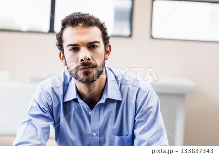 Man sitting on chair in modern office wearing light blue dress shirt near large windows Man sitting on chair in modern office wearing light blue dress shirt near large windows 133837343