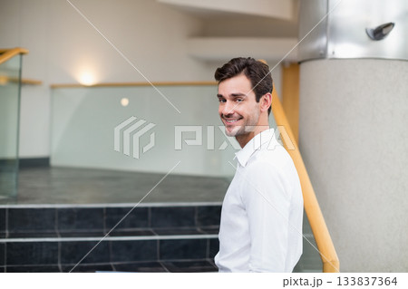 Mid adult man standing near frosted glass panel, handrail by stone staircase in lobby, copy space 133837364