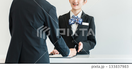 カウンターで手続き,チェックイン,サインする男性と接客対応するホテリエの女性スタッフ 133837983