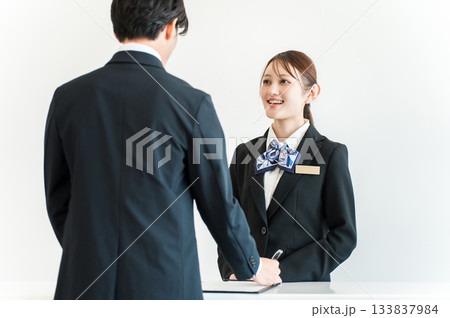 カウンターで手続き,チェックイン,サインする男性と接客対応するホテリエの女性スタッフ 133837984
