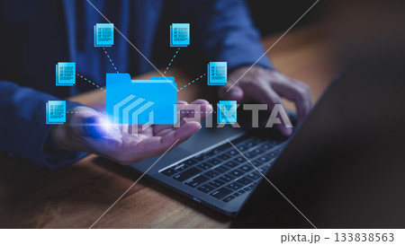 Businessman using laptop computer with glowing blue digital folder and document icons, symbolizing data storage, file management, cloud computing, archiving, and information sharing. Businessman using laptop computer with glowing blue digital folder and document icons, symbolizing data storage, file management, cloud computing, archiving, and information sharing. 133838563