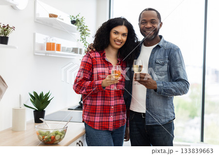 A smiling couple in a kitchen cheers with glasses of wine, celebrating a moment together. A smiling couple in a kitchen cheers with glasses of wine, celebrating a moment together. 133839663