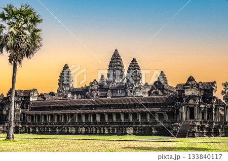 Beautiful sunset view of ancient Angkor Wat temple silhouette with tall palm tree against orange yellow sky background in evening Beautiful sunset view of ancient Angkor Wat temple silhouette with tall palm tree against orange yellow sky background in evening 133840117