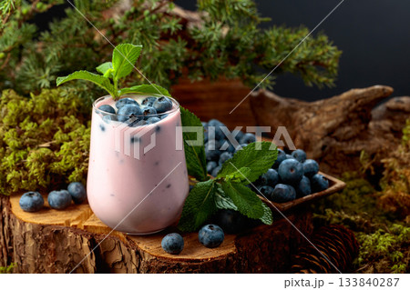 Blueberry smoothie in glass and fresh berries on a pine stump. Blueberry smoothie in glass and fresh berries on a pine stump. 133840287