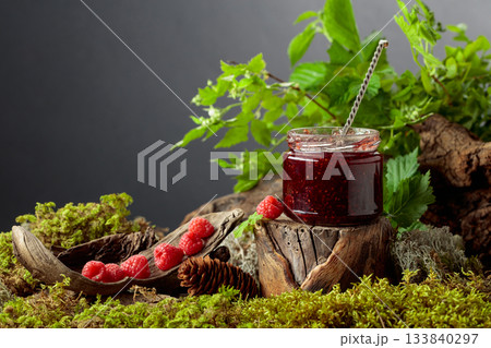 A jar of raspberry jam with fresh berries on an old tree trunk in the forest. A jar of raspberry jam with fresh berries on an old tree trunk in the forest. 133840297