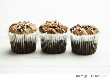 Chocolate cupcakes are showing in flat design on white table with liners, frosting and toppings Chocolate cupcakes are showing in flat design on white table with liners, frosting and toppings 133841262