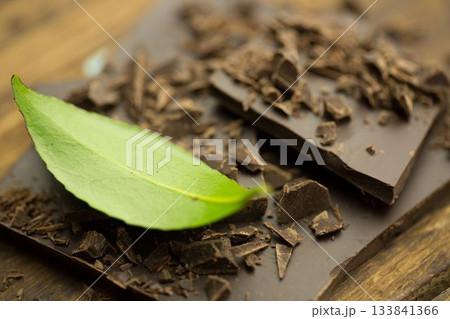 Flat design close-up is showing broken dark chocolate pieces with fresh green leaf on rustic board Flat design close-up is showing broken dark chocolate pieces with fresh green leaf on rustic board 133841366