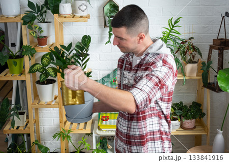 A man takes care of home-made potted plants on the shelves, waters from a watering can, his business 133841916