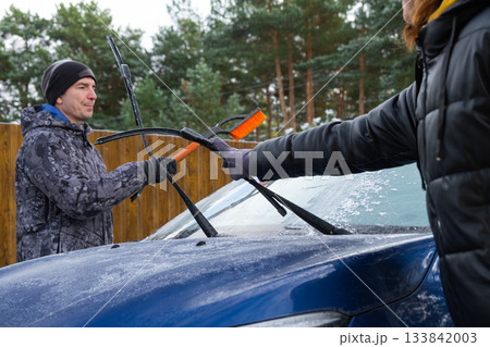 Husband and wife clean the car of ice from near the house in the yard in the autumn frosts 133842003
