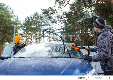 Husband and wife clean the car of ice from near the house in the yard in the autumn frosts Husband and wife clean the car of ice from near the house in the yard in the autumn frosts 133842004