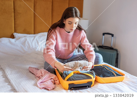 Woman packing suitcase on bed in hotel room Woman packing suitcase on bed in hotel room 133842019