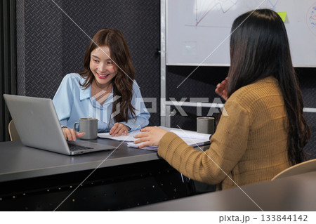 Business women meet, busy team people discuss important project work, meeting plans in modern conference room, smiling woman points to laptop screen during active collaboration. Business women meet, busy team people discuss important project work, meeting plans in modern conference room, smiling woman points to laptop screen during active collaboration. 133844142