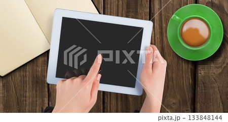 Hands are holding white tablet over wood table in flat design, showing open notebook, coffee 133848144