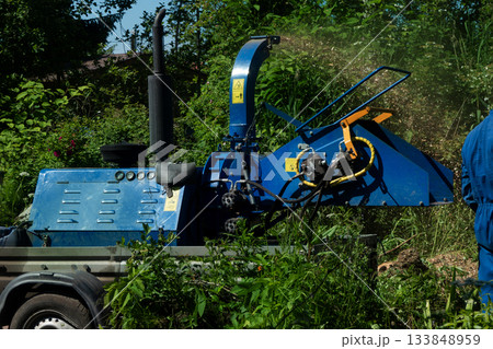 An operator loads tree branches into a wood chipper. 133848959
