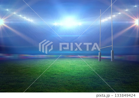 Rugby goalposts with padded bases are standing on floodlit turf at night, floodlights are glowing 133849424