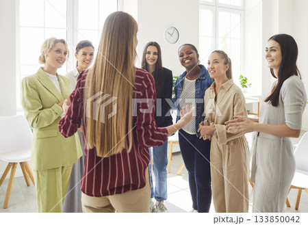 Group of women standing in bright office, listening to their colleague, engaging in discussion. 133850042