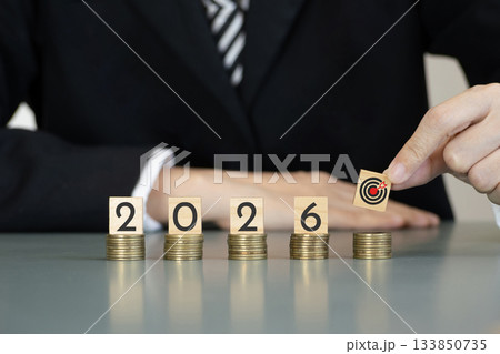 business people places a target block on stacks of coins beside number of year 2026 on wooden cubes, symbolizing investment strategy, financial planning, revenue goals, growth, execution, success 133850735