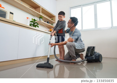 Family bonding through cleaning. Father and son vacuuming together in modern kitchen. Family bonding through cleaning. Father and son vacuuming together in modern kitchen. 133850835