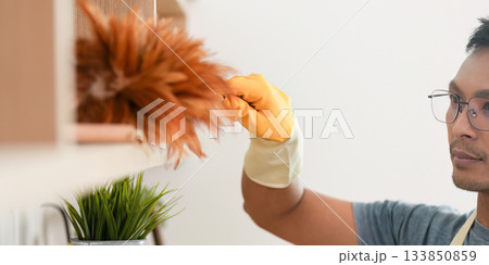 Home Cleaning. Man dusting shelves with yellow gloves. Home Cleaning. Man dusting shelves with yellow gloves. 133850859